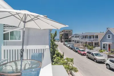 a balcony with an umbrella and a street with parked cars at Upgraded 5Br Summer Vacation Home, Steps From The Sand By Beachview Rentals in Newport Beach