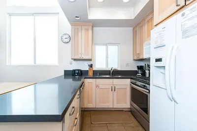 a kitchen with white appliances and wooden cabinets at Modern Oceanview Tri-Level Condo Steps From The Beach By Beachview Rentals in Newport Beach