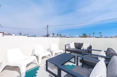 a patio with white chairs and furniture on a roof at Modern Oceanview Tri-Level Condo Steps From The Beach By Beachview Rentals in Newport Beach
