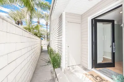 a white house with a door and palm trees at Updated 3Br Beach Home W Patio And Bbq, In Prime Location By Beachview Rentals in Newport Beach