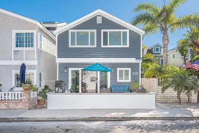 a gray house with a blue umbrella in front of it at Updated 3Br Beach Home W Patio And Bbq, In Prime Location By Beachview Rentals in Newport Beach