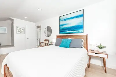 a white bedroom with a large white bed with blue pillows at Updated 3Br Beach Home W Patio And Bbq, In Prime Location By Beachview Rentals in Newport Beach