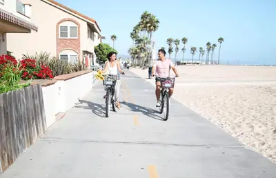 two people riding bikes down a sidewalk on the beach at Luxury 4Br Tri-Level W Modern Interior, Rooftop Deck, Ac By Beachview Rentals in Newport Beach