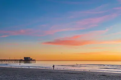 a person standing on a beach with a pier in the background at Updated 2Br Vintage Cottage In Central Location Near Beach By Beachview Rentals in Newport Beach
