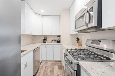 a kitchen with white cabinets and a stove top oven at Cozy Cottage W Ac, Stylish Interior, One House From Beach By Beachview Rentals in Newport Beach