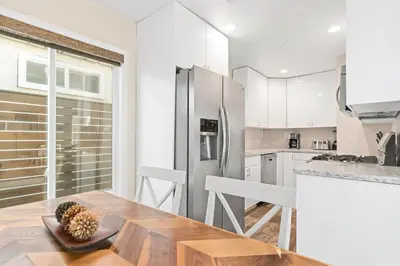 a kitchen with a wooden table and a refrigerator at Cozy Cottage W Ac, Stylish Interior, One House From Beach By Beachview Rentals in Newport Beach