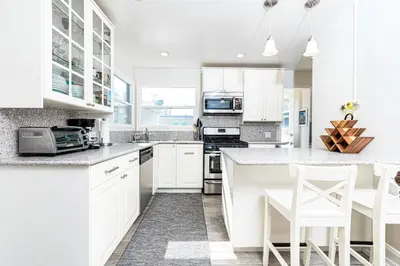 a white kitchen with white cabinets and white appliances at Cozy 2Br W Large Deck, Steps From Marina Park And Beach By Beachview Rentals in Newport Beach