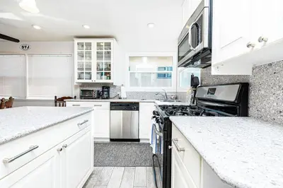 a white kitchen with white cabinets and appliances at Cozy 2Br W Large Deck, Steps From Marina Park And Beach By Beachview Rentals in Newport Beach