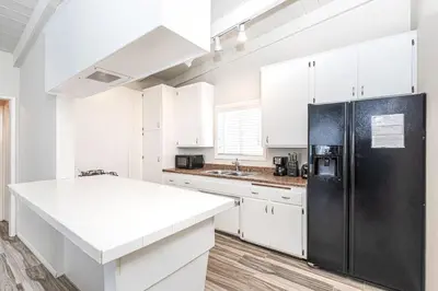 a kitchen with white cabinets and a black refrigerator at Cozy 2Br Upstairs Cottage Steps From Sand In Prime Location By Beachview Rentals in Newport Beach