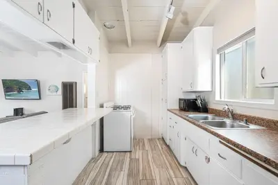 a white kitchen with white cabinets and a sink at Cozy 2Br Upstairs Cottage Steps From Sand In Prime Location By Beachview Rentals in Newport Beach