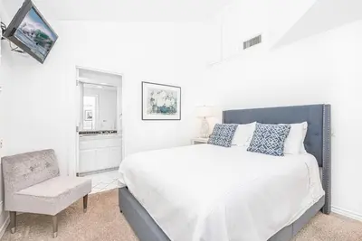 a white bedroom with a large bed and a chair at Luxe Oceanfront 3Br W Rooftop Deck, Pier To Pier Location By Beachview Rentals in Newport Beach