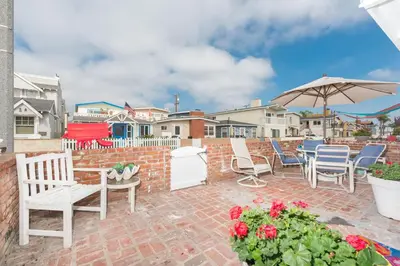 a patio with chairs and an umbrella and flowers at Charming 1Br Beach Cottage W Large Patio One Block To Sand By Beachview Rentals in Newport Beach
