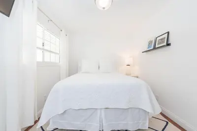 a white bedroom with a white bed and a window at Charming 1Br Beach Cottage W Large Patio One Block To Sand By Beachview Rentals in Newport Beach