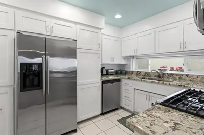 a kitchen with white cabinets and a stainless steel refrigerator at Affordable 3Br Near Beach, Walk To Shops, Dining And More By Beachview Rentals in Newport Beach