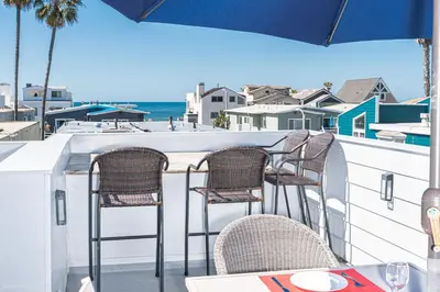 a table and chairs on a balcony with a view of the ocean at Updated 3Br W Oceanview Rooftop Deck, Steps To The Beach By Beachview Rentals in Newport Beach