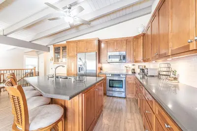 a large kitchen with wooden cabinets and a large island at Charming 2Br Condo W Ac, Steps To Beach And Balboa Pier By Beachview Rentals in Newport Beach