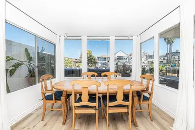 a dining room with a table and chairs and windows at 3Br Bayfront W Expansive Front Patio - Easy Walk To Beach By Beachview Rentals in Newport Beach