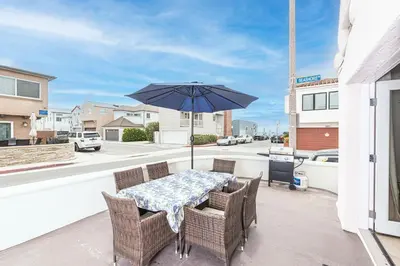 a table and chairs with an umbrella on a balcony at Steps To Sand! 7Br Retreat W Ocean Views In Prime Location By Beachview Rentals in Newport Beach