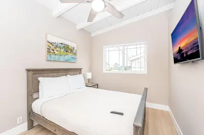 a bedroom with a bed and a tv on the wall at Stylish 6Br Duplex, One Block From Beach And Boardwalk By Beachview Rentals in Newport Beach