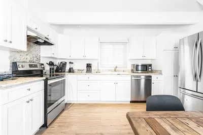 a white kitchen with white cabinets and a wooden floor at Updated 2Br Cottage One House From Beach - Super Central By Beachview Rentals in Newport Beach