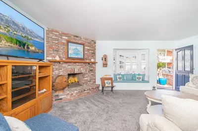 a living room with a brick fireplace and a tv at Roomy 2Br W Large Patio, Fire Pit And Ocean Views By Beachview Rentals in Newport Beach