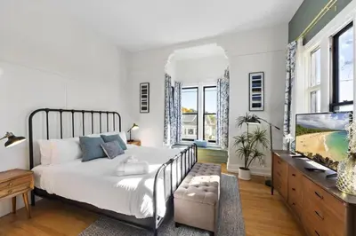 a white bedroom with a bed and a tv at Victorian Gem Close to Petco Park & Gaslamp in San Diego