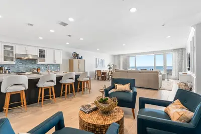 a living room with blue chairs and a kitchen at The Penthouse Oceanfront in Oceanside