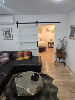 a living room with a black leather couch and a bedroom at Cozy IBR with Bathtub Hot Tub, Near Golf, Beach, TJ in Bonita