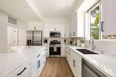 a white kitchen with white cabinets and a large window at Coastal Ocean Beach Compound Escape in San Diego