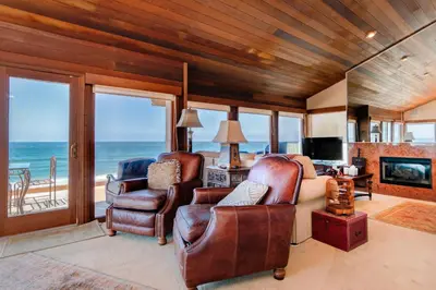 a living room with two chairs and a television and the ocean at Luxury Oceanfront Home- Upper in Oceanside