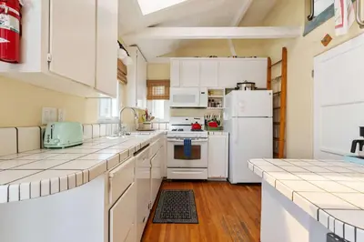 a white kitchen with white appliances and wooden floors at Cute Home Steps from the Sand in San Diego