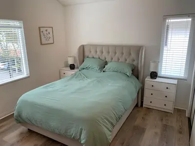 a bedroom with a bed with green sheets and two windows at Beautifully Remodeled 2BR Prime Irvine Location in Irvine