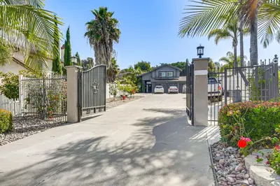 a gate to a driveway with a house and palm trees at Pool Access and Private Deck Mtn-View Bonita Studio in Bonita