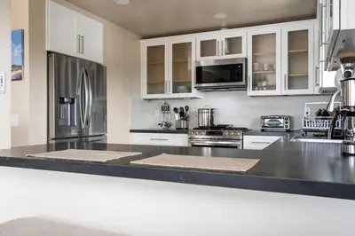 a kitchen with white cabinets and a stainless steel refrigerator at New Cozy Leucadia Beach House with parking in Encinitas