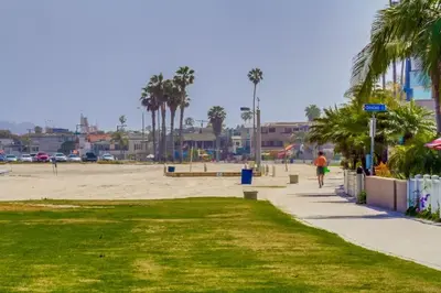 a person walking down a sidewalk next to a beach at Bayside Gem - Beachfront - Vibrant - Ocean Breeze in San Diego