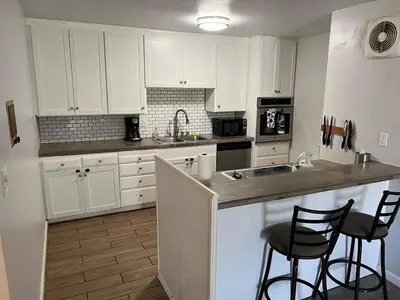 a kitchen with white cabinets and two bar stools at Sunny Condo Steps from Sand in San Diego
