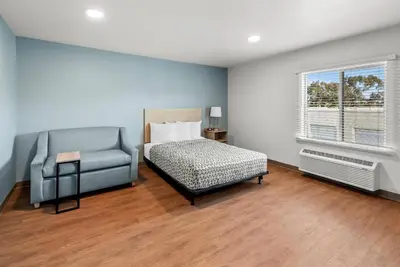 a bedroom with a bed and a chair and a window at WoodSpring Suites Santee - San Diego Northeast in Santee