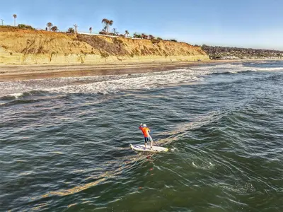 a person standing on a surfboard in the water at Solana Oceanfront with Pool, Spa, Ocean Views in Solana Beach