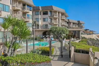 an apartment building with a swimming pool and palm trees at Solana Oceanfront with Pool, Spa, Ocean Views in Solana Beach