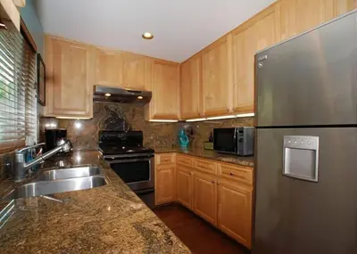 a kitchen with wooden cabinets and a stainless steel refrigerator at Get Your Vitamin Sea! Steps to beach! Fire pit! in Newport Beach