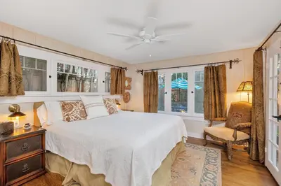 a bedroom with a bed and a chair and windows at Seahorse Cottage in Secret Garden Sanctuary in San Diego