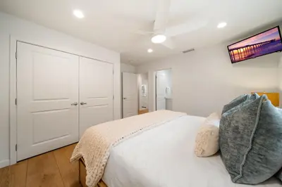 a white bedroom with a bed and a tv on the wall at OB Cottage Beach Views in San Diego