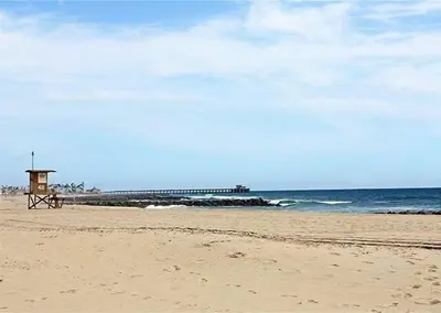 a bench on a beach with a pier in the background at 6BR Beach House w/ Bikes/Fire pit/BBQ/Easy Parking in Newport Beach