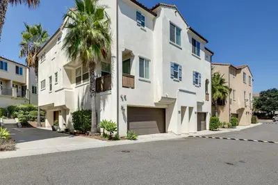 a white building with a palm tree next to a street at Walk to Public Transit Oceanside Home with Balcony in Oceanside