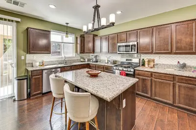 a kitchen with wooden cabinets and a island with bar stools at Spacious Menifee Home with Patio, 9 Mi to Lake! in Menifee