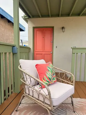 a wicker chair sitting on a porch with a red door at Catch of the Day Pet-Friendly El Pescador 1 Block from the Beach in San Diego