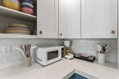 a kitchen with white cabinets and a microwave on a counter at Steps to Lido Village and the Marina Heart of Lido Island 2 Car Garage in Newport Beach