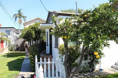 a white fence in front of a house with an orange tree at Sweet n Cozy Cottage near Little Italy & Gaslamp in San Diego
