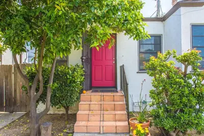 a red door on a white house with trees at Cozy Urban Cottage in San Diego