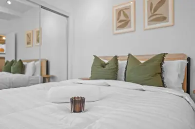 a white bed with green pillows and a cup on it at Modern Eclectic 2BR Near Petco, Balboa Park & Zoo in San Diego